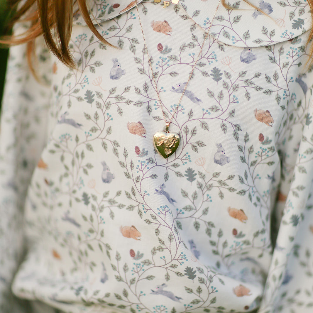 A gold heart locket on a chain, worn over a floral blouse