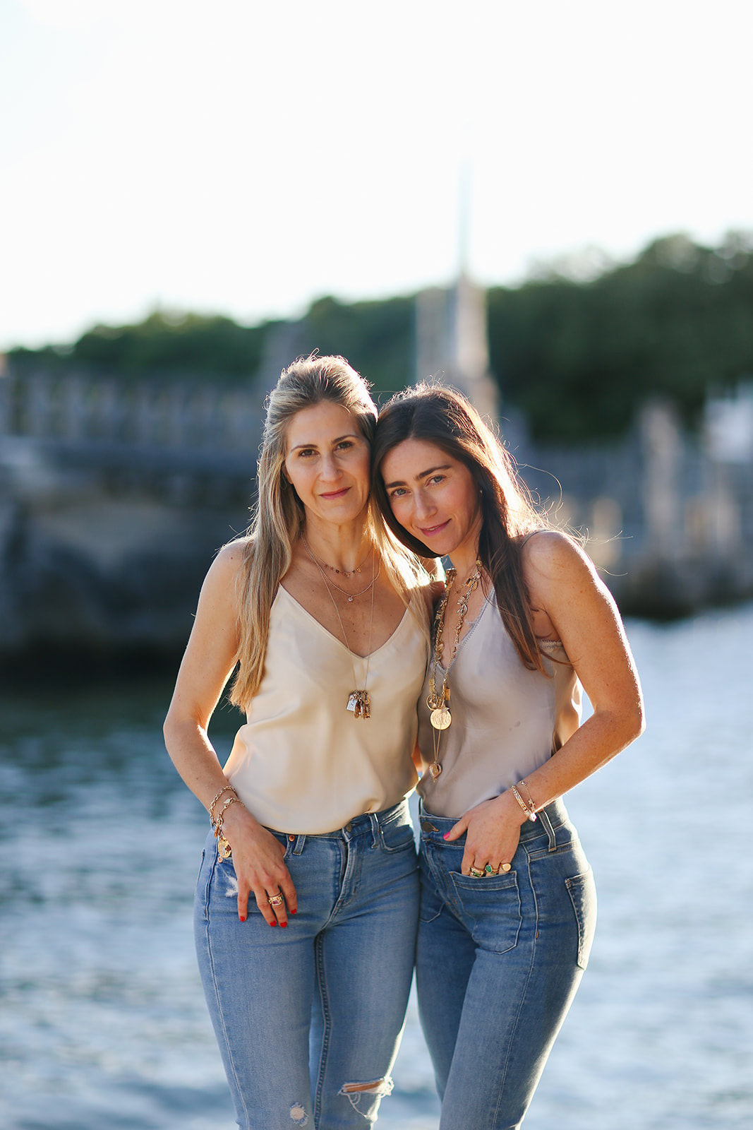 Emily and Ashley Green at the water at golden hour, wearing their gold charm necklaces