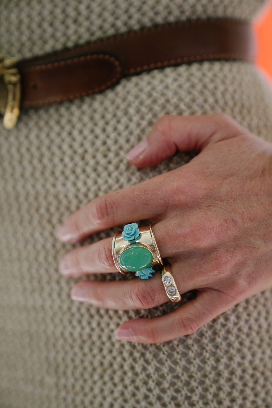 Gold and gemstone rings on the hand, with a green raffia bag