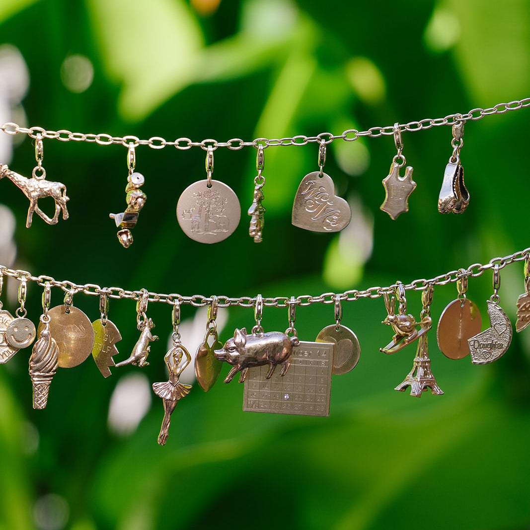 Emily and Ashley 14k gold charm bracelets hanging against green leaves