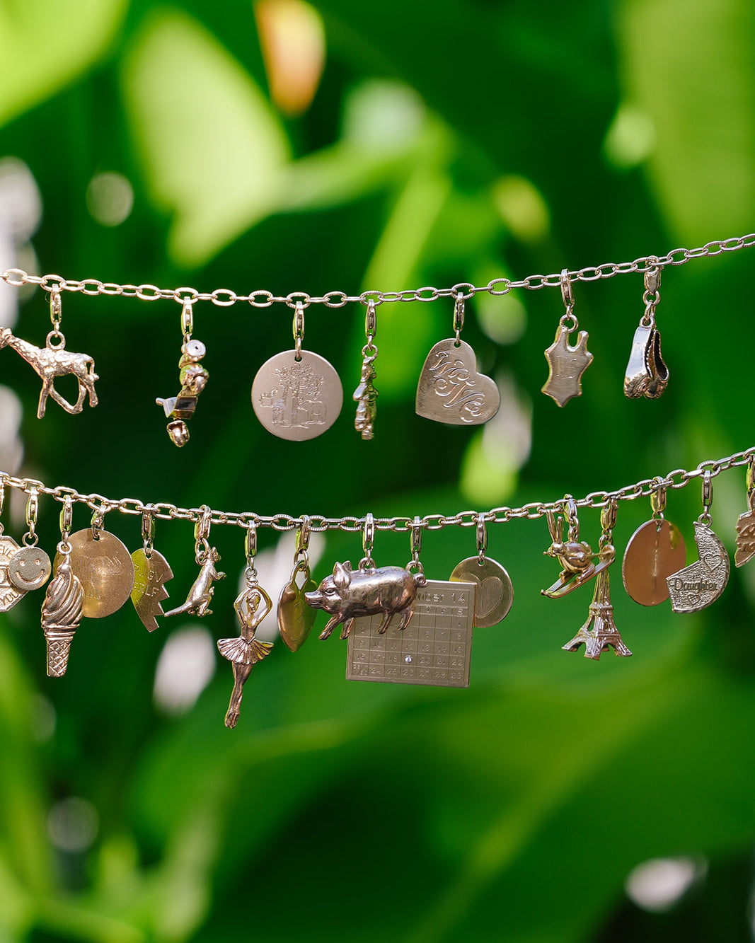 Emily and Ashley 14k gold charm bracelets hanging against green leaves