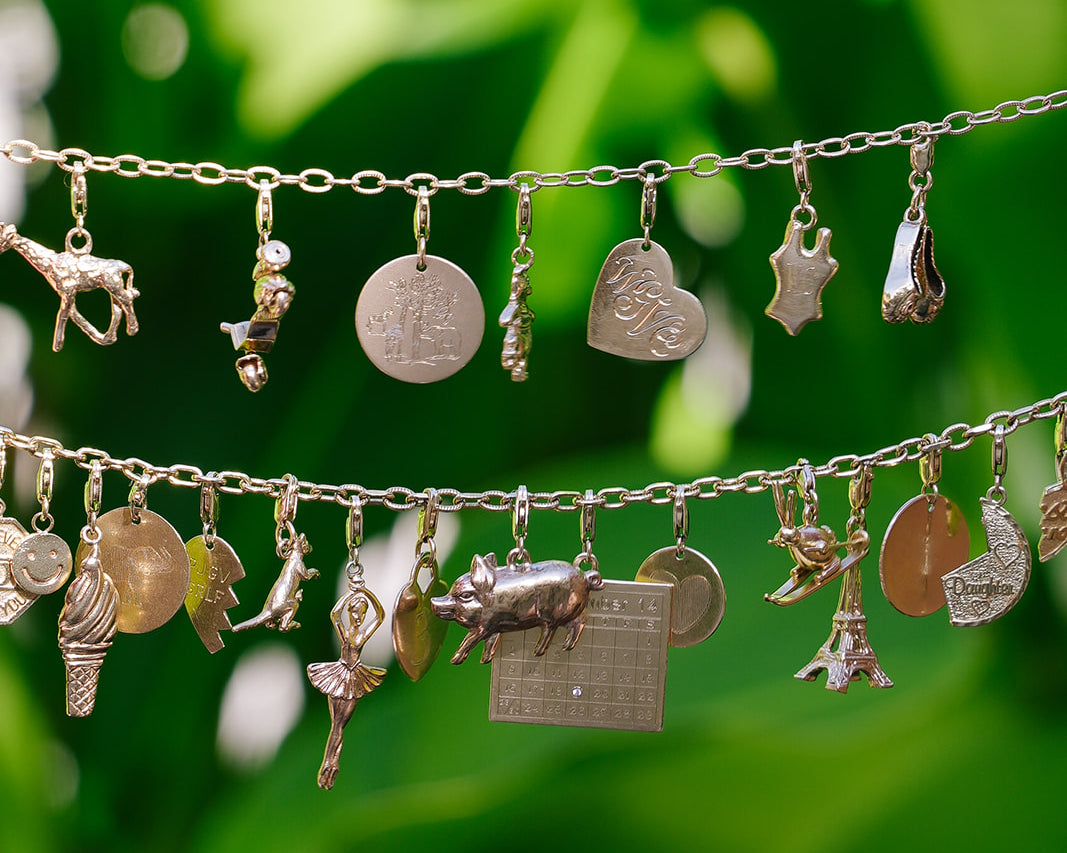Emily and Ashley 14k gold charm bracelets hanging against green leaves