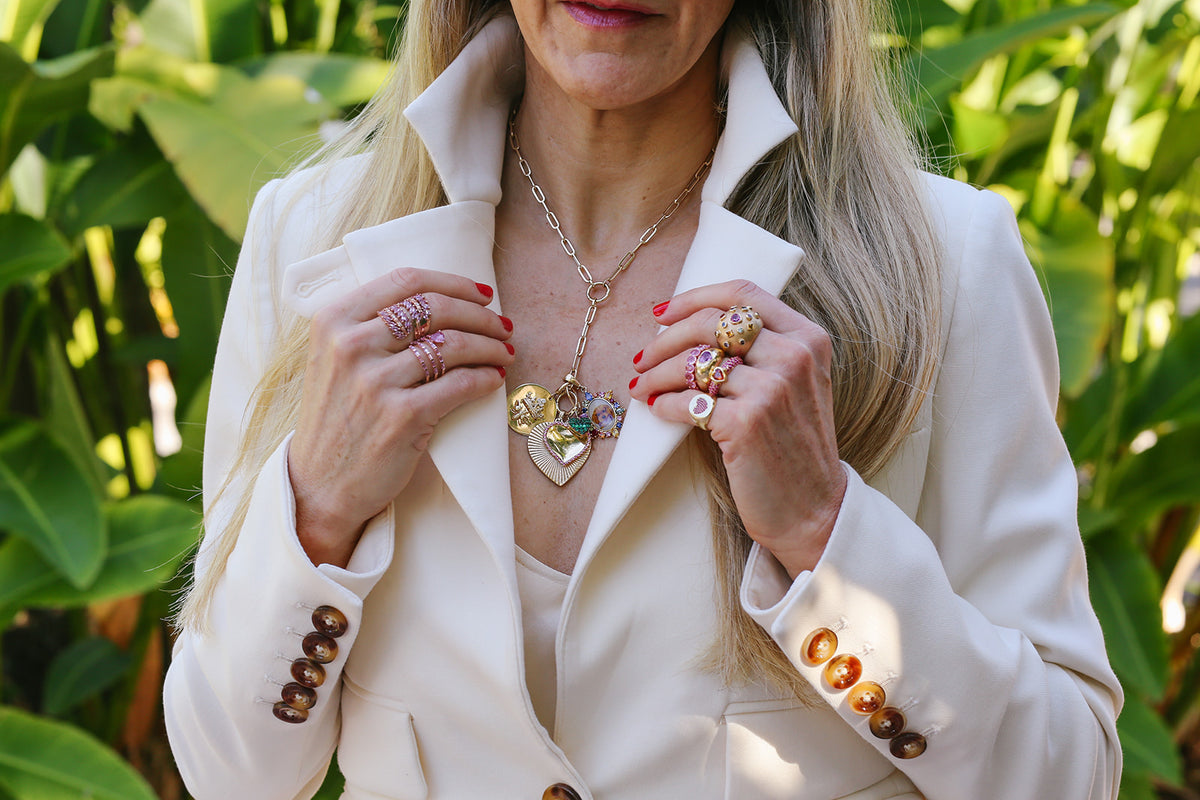 Layered gold charm necklaces and rings worn with a white blazer