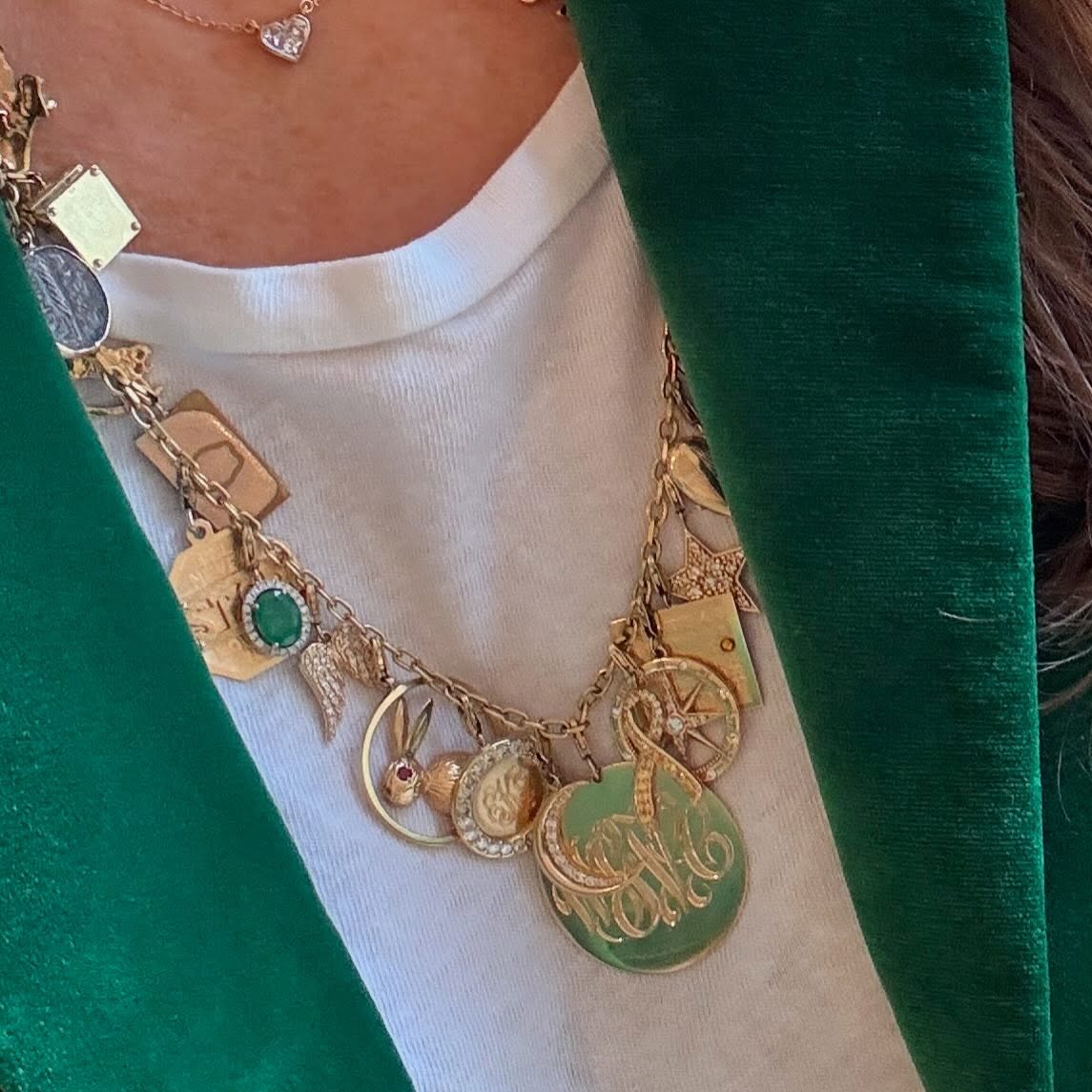 A gold charm necklace with an engraved monogram disc over a green velvet jacket